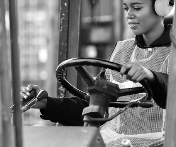 Close-up of young woman wearing noise protection ear muffs driving a forklift in a warehouse